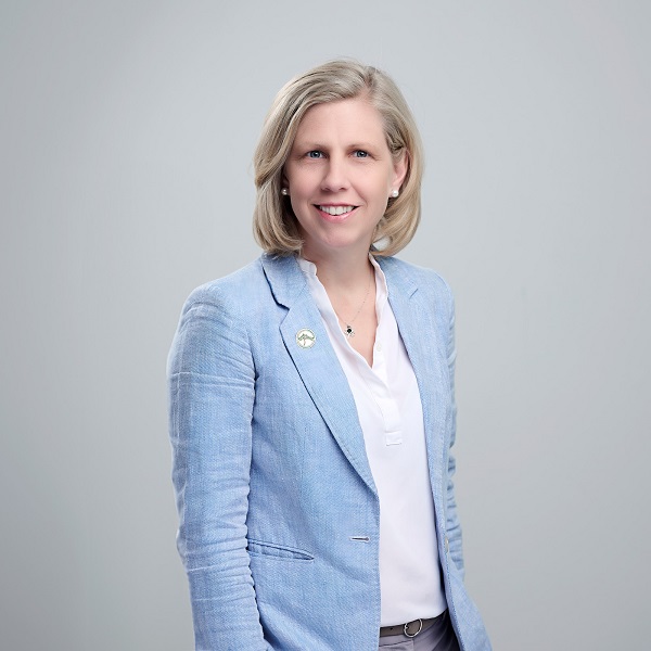 A woman in a blue jacket and a white shirt stands and smiles