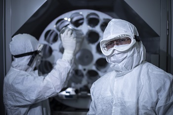 Two people wear full-body protective suits in a lab.