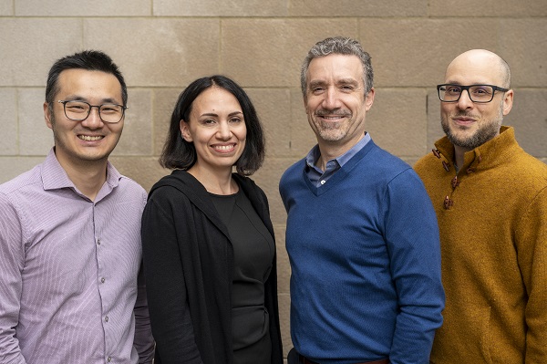 Four researchers stand against a wall, smiling.