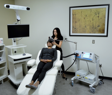 A woman holds a medical device over another women's head in a clinical environment.