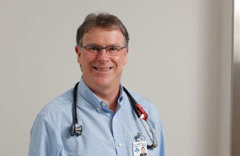 a person in a blue shirt and glasses stands in front of a white wall